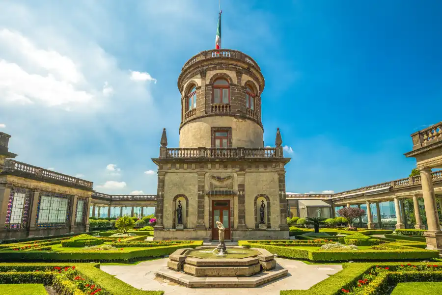 Central tower of Chapultepec Castle with manicured gardens, fountains, and blue sky.