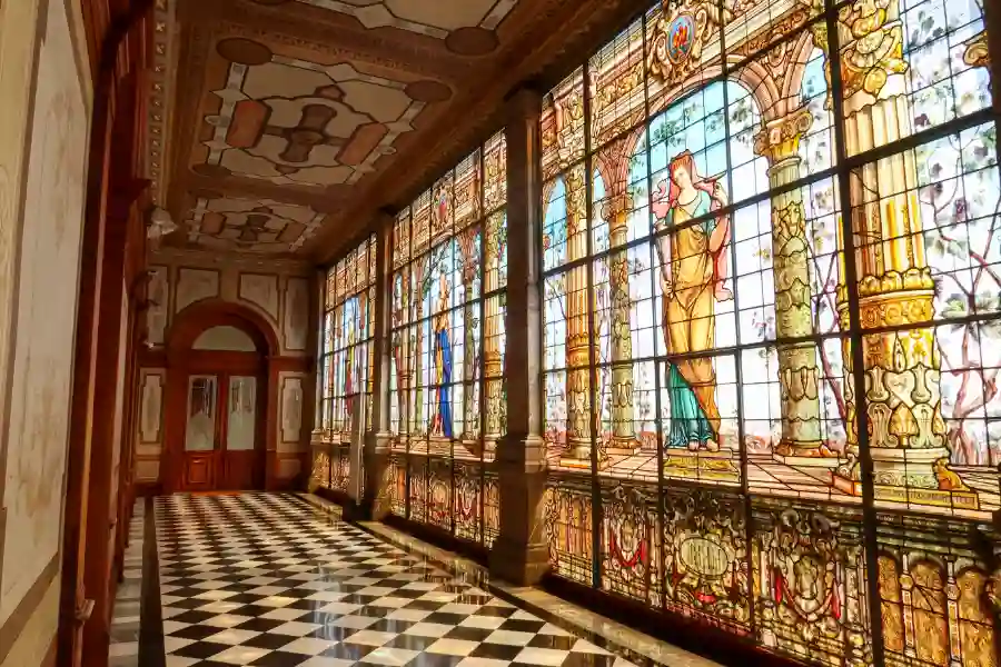 Stained glass windows with classical figures inside Chapultepec Castle, along a checkered hallway, during a private museum tour in Mexico City.