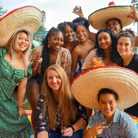 Group of friends wearing sombreros and celebrating with drinks on a colorful trajinera boat in the canals of Xochimilco, Mexico City.