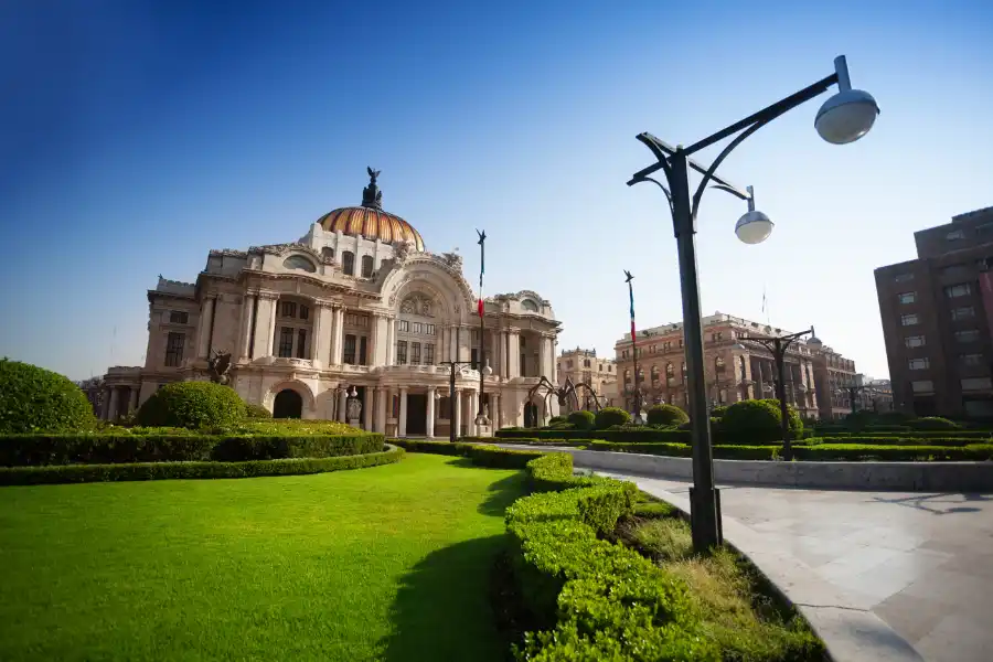 Palacio de Bellas Artes with manicured gardens and blue sky in Mexico City.