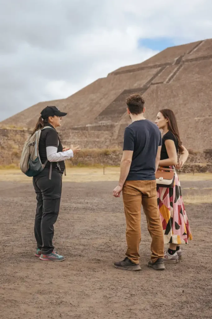 A female guide with a backpack talking to a man and woman in front of the Pyramid of the Sun in Teotihuacán during a private tour.