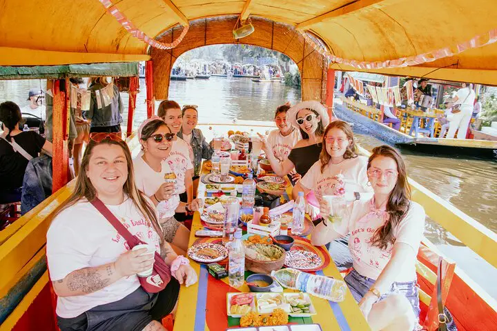 Group of women enjoying food and drinks on a exclusive boat party aboard a colorful trajinera in Xochimilco canals.
