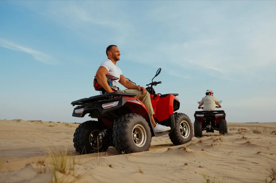 Local ATV tour guide resting on a red quad in the Baja desert with a rider in the background.