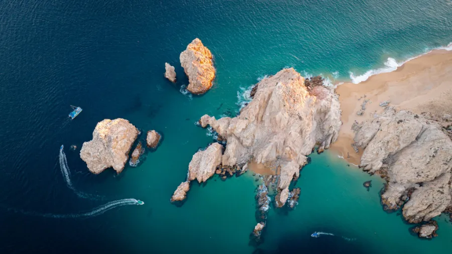 Aerial view of Land’s End rock formations and Arch of Cabo San Lucas with turquoise water, boats, and sandy beach in Baja California Sur.