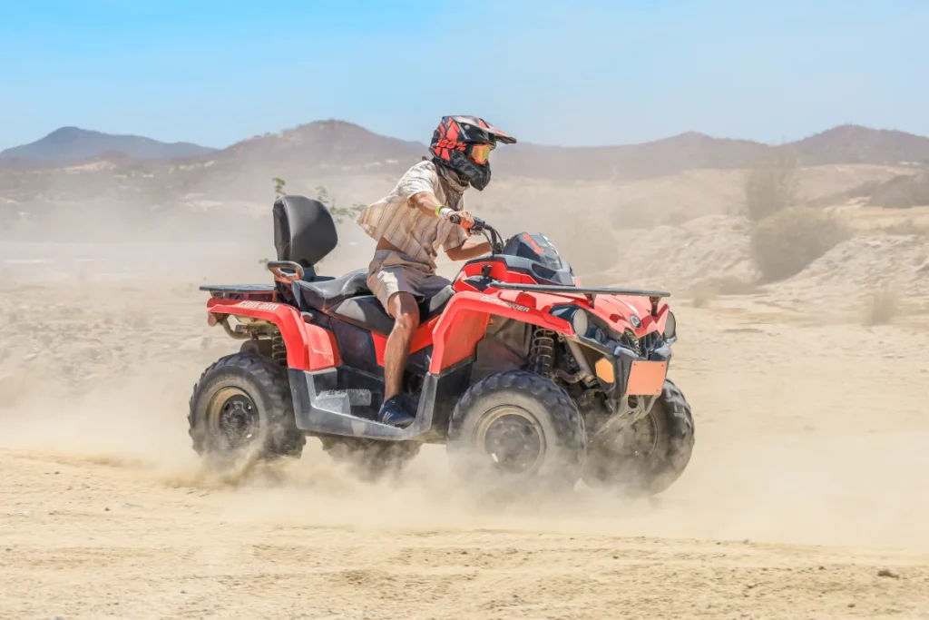Rider driving an ATV through the desert landscape of Cabo San Lucas with dust trails and mountain scenery.