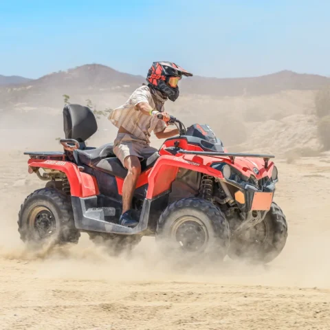 Rider driving an ATV through the desert landscape of Cabo San Lucas with dust trails and mountain scenery.