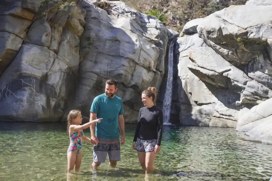 Family enjoying natural pool next to waterfall in Fox Canyon in Los Cabos.