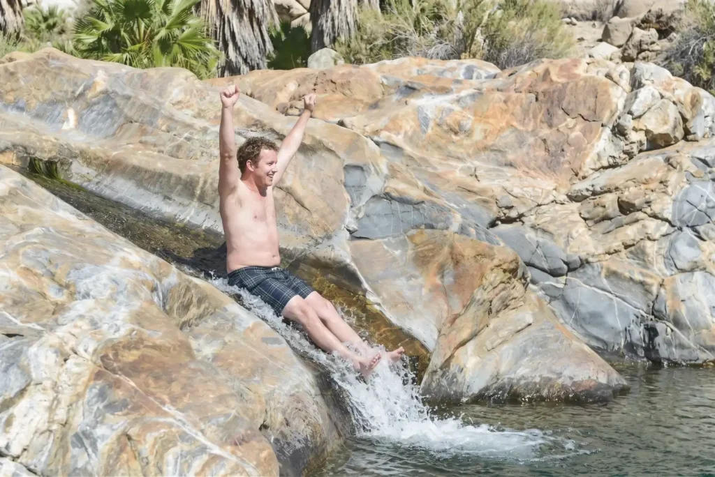 Man sliding down natural rock waterslide with arms raised at Fox Canyon in Cabo San Lucas.