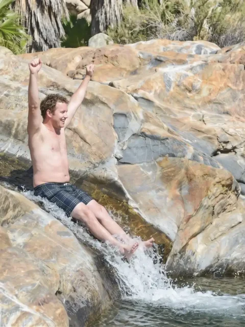 Man sliding down natural rock waterslide with arms raised at Fox Canyon in Cabo San Lucas.