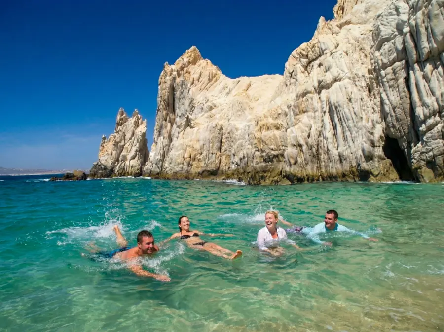 Group of friends swimming in clear turquoise water near the Arch at Cabo San Lucas.