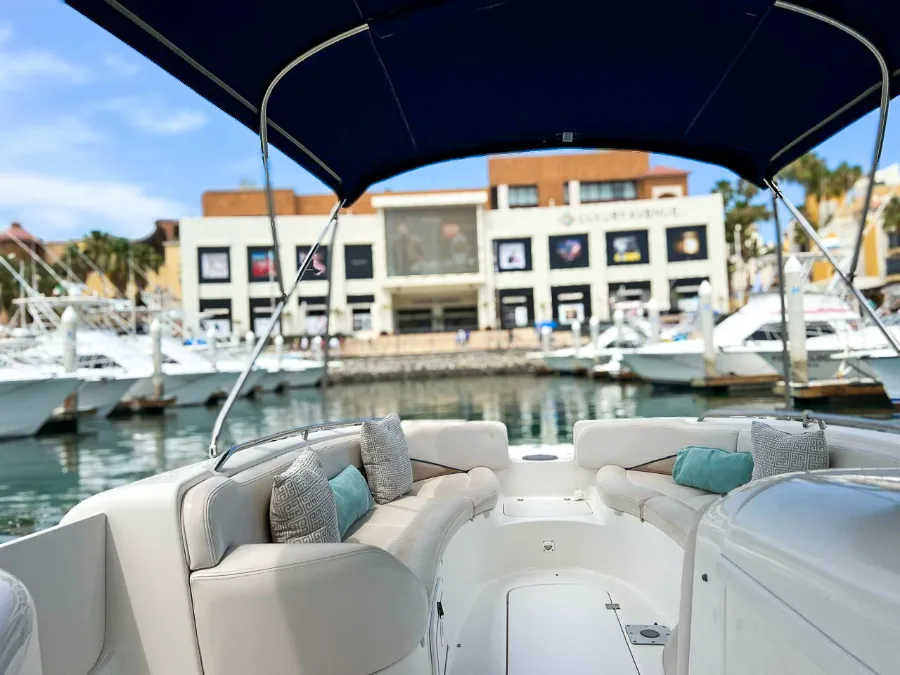 Luxury boat interior docked at Los Cabos Marina with waterfront restaurants and yachts in the background.