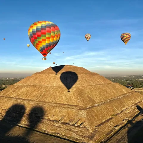 Colorful hot air balloons drifting over the Teotihuacan archaeological site near Mexico City, with ancient pyramids and historic ruins at sunrise.