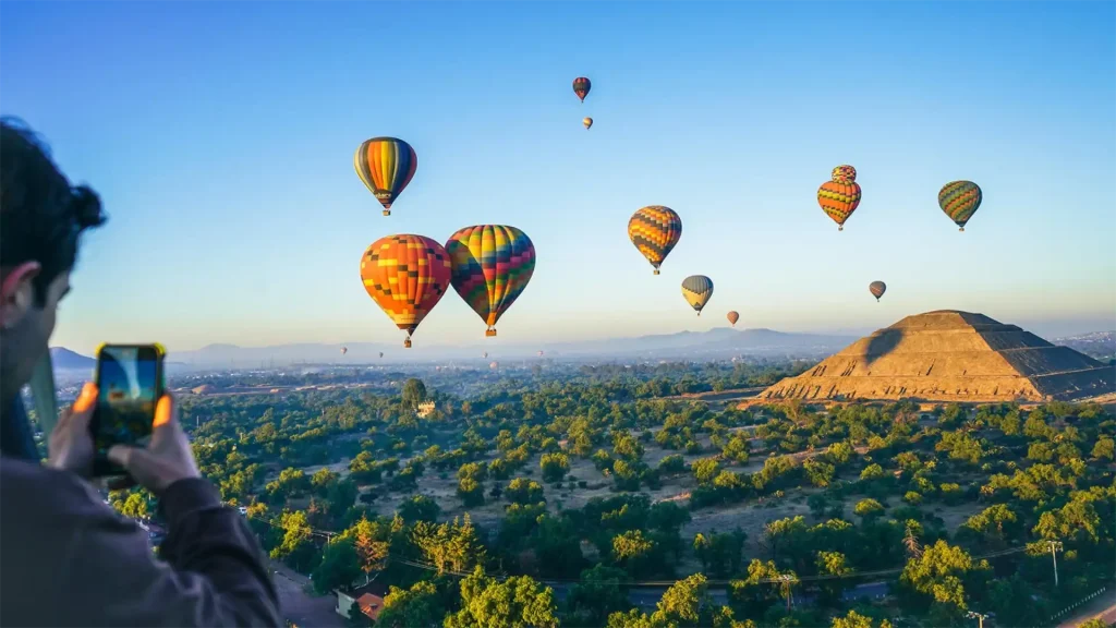 Multiple hot air balloons floating above the Pyramid of the Sun in Teotihuacan during sunrise.