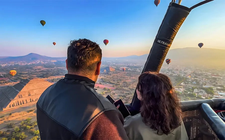 Couple enjoying a Mexico City hot air balloon ride over Teotihuacan with pyramids and sunrise views below.