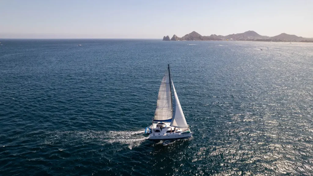 Private catamaran sailing across the Sea of Cortez with the Cabo San Lucas coastline in the distance.