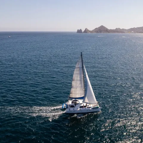 Private catamaran sailing across the Sea of Cortez with the Cabo San Lucas coastline in the distance.