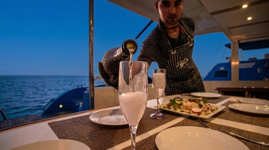 Crew member serving champagne during an all-inclusive private catamaran sailing tour in Cabo San Lucas.