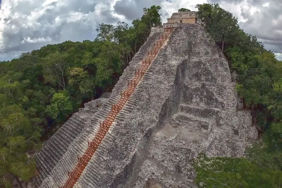 Nohoch Mul pyramid at Coba ruins with wooden staircase above the jungle canopy
