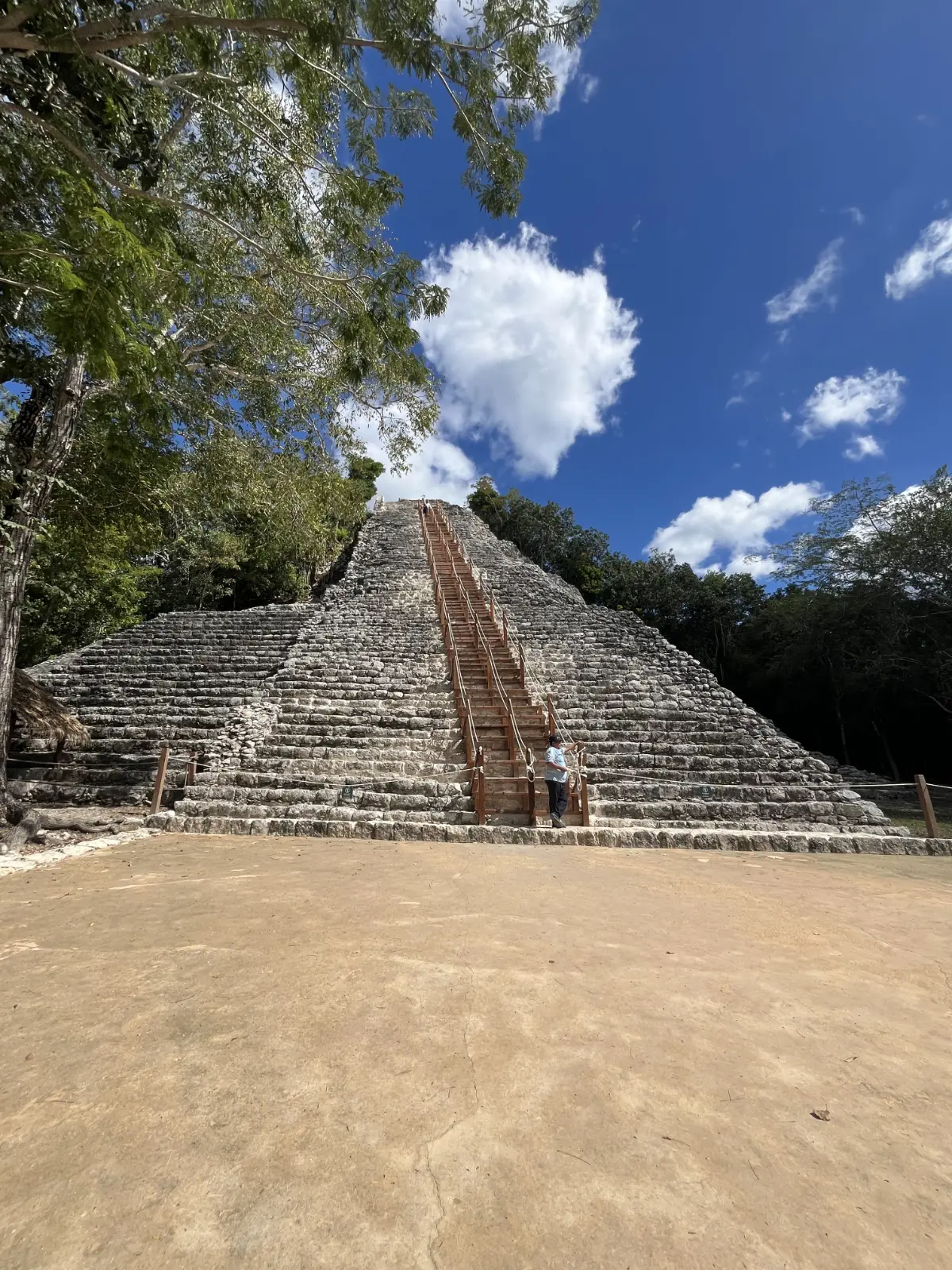 Nohoch Mul pyramid at Coba ruins with wooden staircase and visitor at the base.