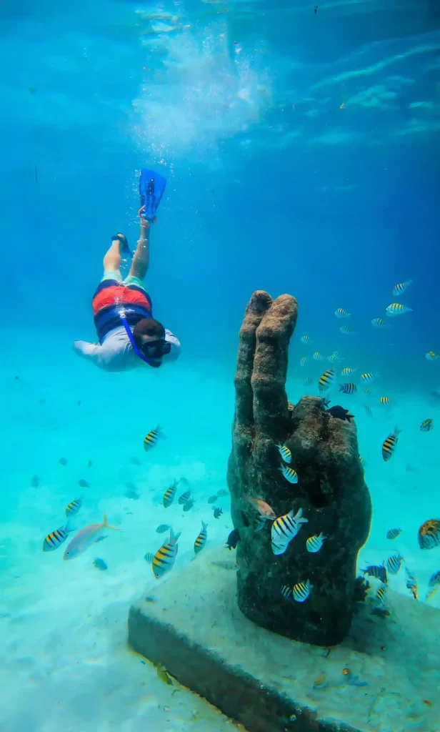 Snorkeler diving near a submerged stone sculpture surrounded by tropical fish near Isla Mujeres