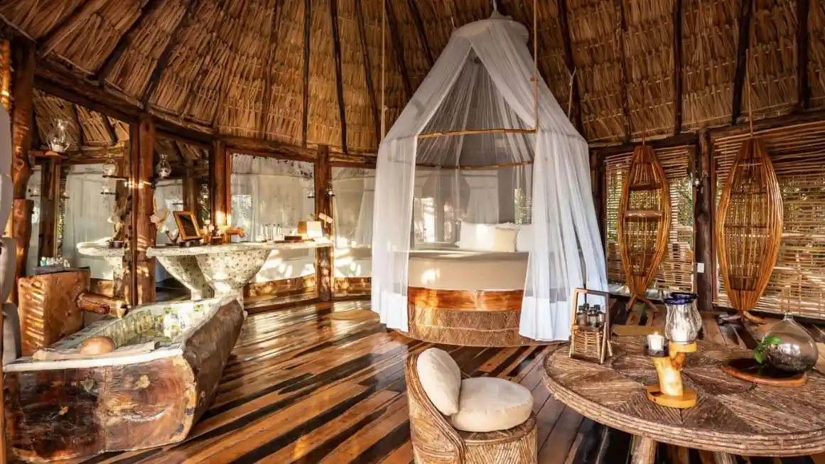 Angle view of a cozy Tulum hotel cabaña room featuring intricate macramé decorations and rustic wooden furniture.