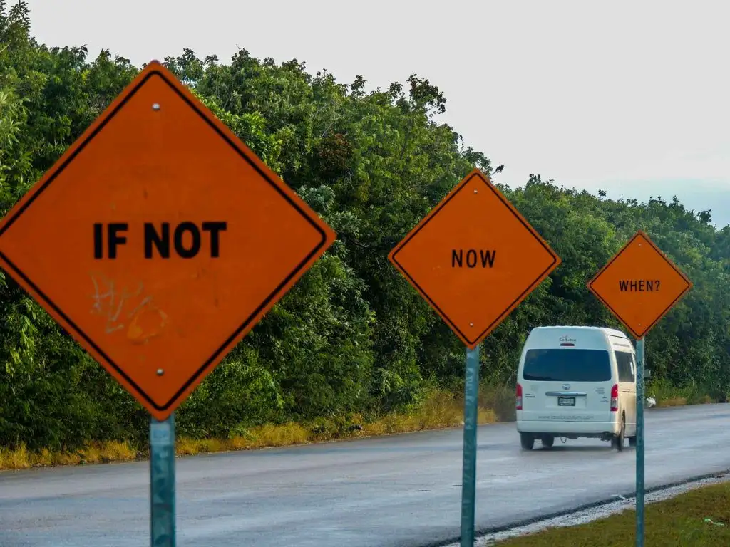 A Toyota van driving along the Tulum highway, passing a billboard with the inspirational slogan 'If not now, when?