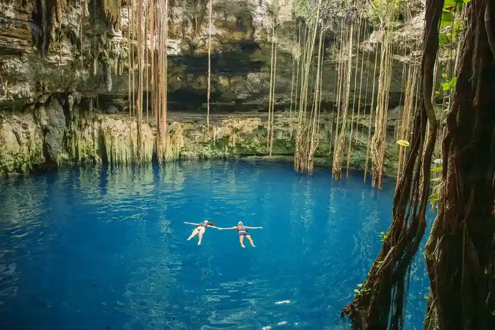 Two tourists are floating in the vivid blue waters of a cenote in Yucatan.