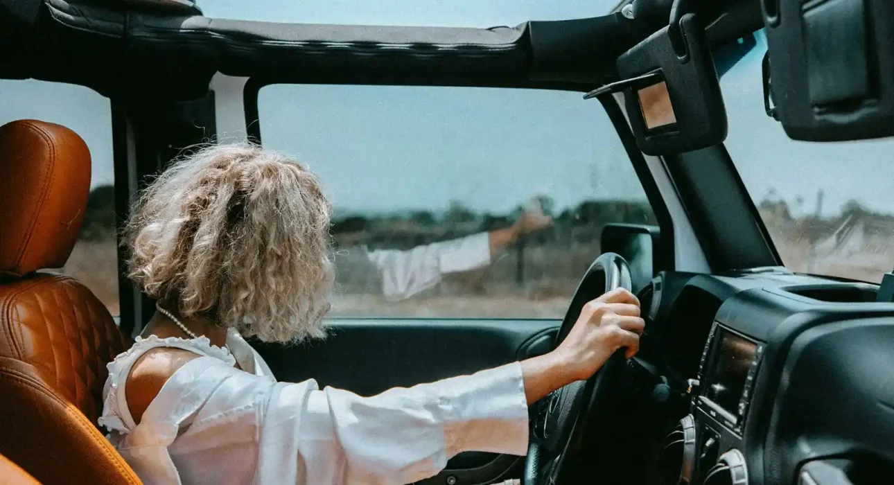 Woman driving a Jeep with the top down on a rural road.