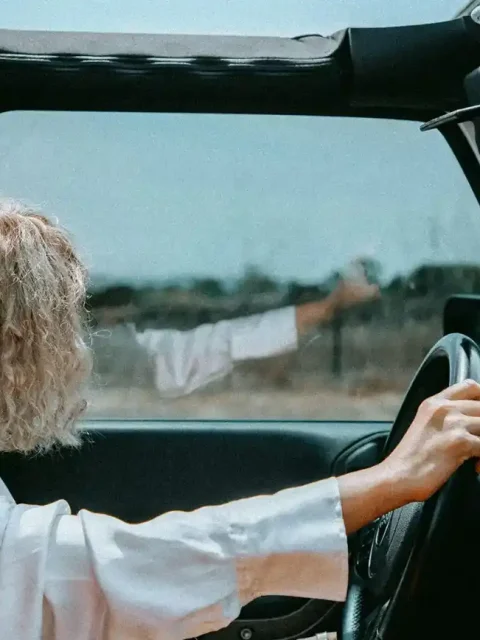 Woman driving a Jeep with the top down on a rural road.