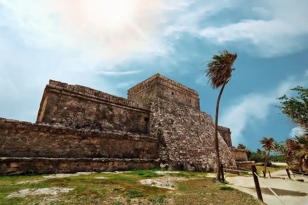 Mayan ruin in Tulum, Mexico, showcasing a large stone structure surrounded by palm trees and sandy pathways.
