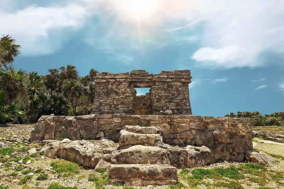 Historic Mayan temple structure in Tulum, Mexico, set against a bright blue sky.